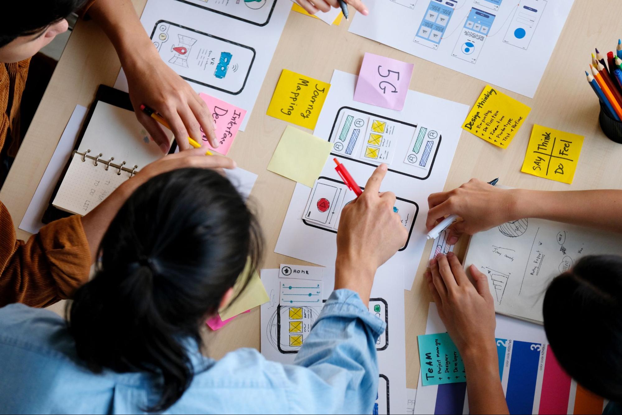 Stock photo showing an overhead view of four co-workers collaborating on sketches of a mobile app