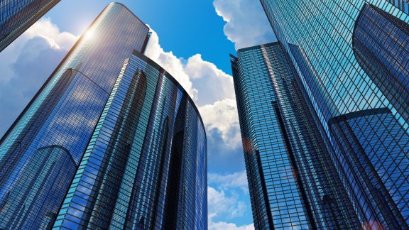 Downtown corporate business district architecture: glass reflective office buildings against blue sky with clouds and sun light