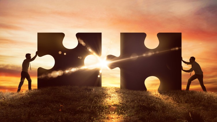 Men push two puzzle pieces at sunset