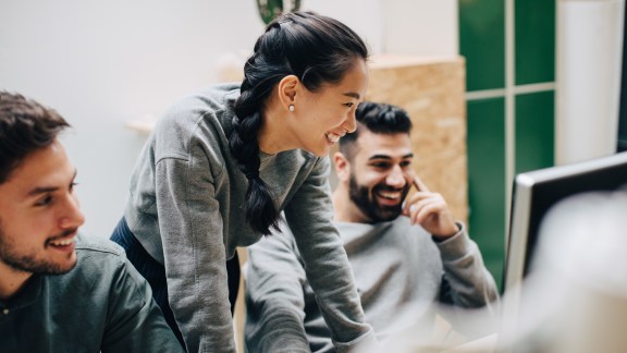 Smiling colleagues looking at computer while working in office - stock photo