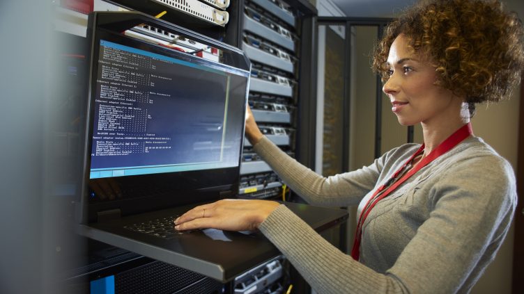 a female IT technician is editing the programme on the network server in a server room. ** all identifying script and racking has been modified **