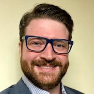 A person with beard and blue glasses smilingDescription automatically generated with low confidence
