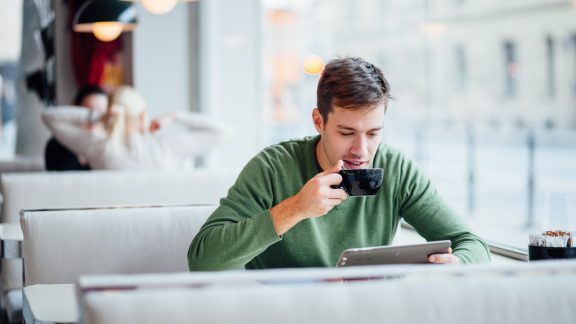 Young man drinking coffee on the street while using tablet computer