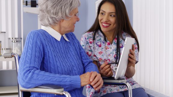 Friendly Mexican caregiver talking to elderly patient with tablet