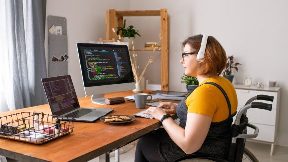 Smart disabled coder sitting in wheelchair and using computers while working from home