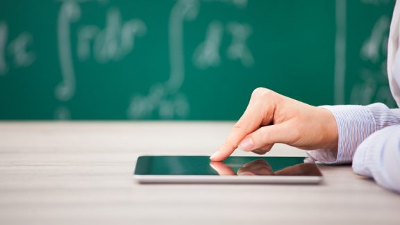 Close-up Of Hand Over Digital Tablet Screen In Front Of Chalkboard