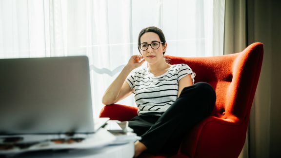 Young woman sitting down watching a movie on her laptop in a contemporary hotel room.