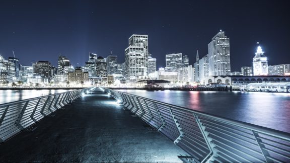 empty footpath over water to modern building in San Francisco at night