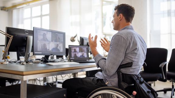 Businessman with disability talking on video call at office. Businessman on a wheelchair having a web conference on his computer at creative office desk.
