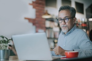 Asian man in button-down shirt in front of laptop screen