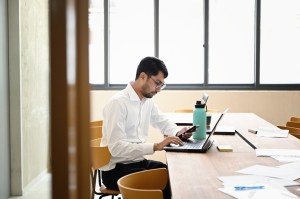 Man working on mobile device and laptop