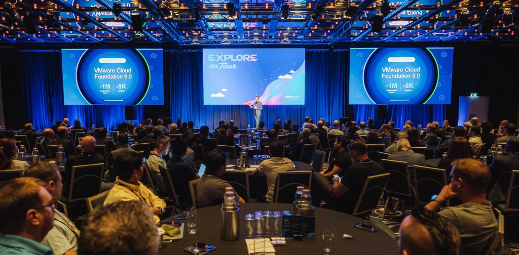 Large crowd of attendees at the Plenary Session at Explore on Tour in Sydney with VCF content on display