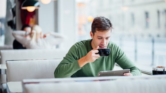 Young man drinking coffee on the street while using tablet computer