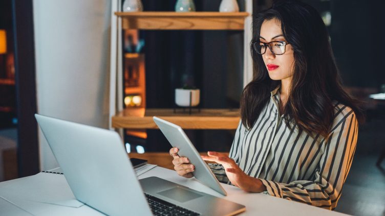 Shot of a young businesswoman using a digital tablet and laptop during a late night at work