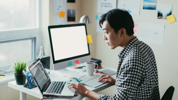 Man looking at computer code on a laptop while working from his small office.