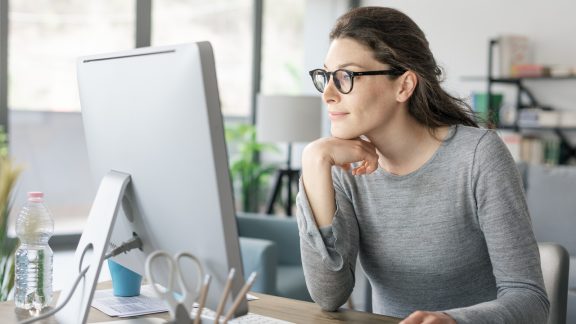 Professional woman sitting at desk and connecting with her computer, she is looking through her certification options