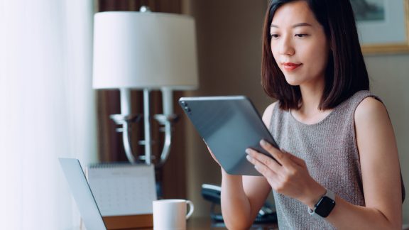 Young Asian businesswoman using digital tablet while sitting at her desk in office. Remote working, freelancer, small business ideas. Female leadership. Making business connections with technology