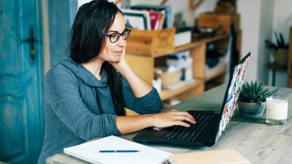 Ethnic simpotic dark-skinned brunette woman working on a laptop in the interior of a cozy living room or kitchen of her apartment. Remote work from home. Individual quarantine isolation.