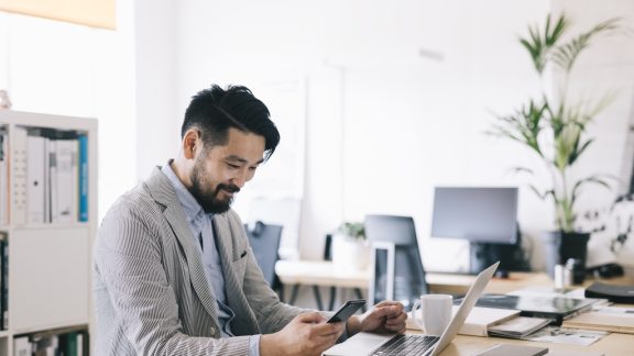 Positive Asian small business owner checking his smartphone at work.