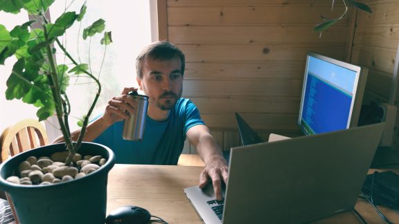 freelance developer or programmer drinks and write code, working from home in quarantine, concept of self-isolated lifestyle workspace or workplace, home office, side view