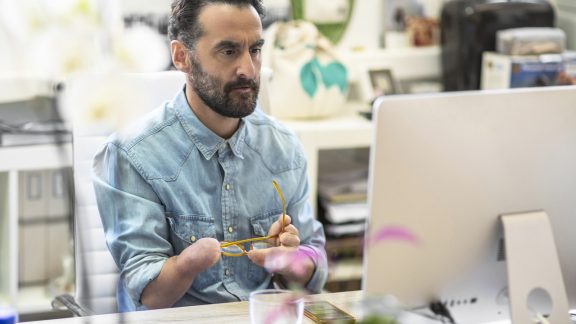 Serious mature businessman looking at computer. Disabled design professional sitting at desk. He is in creative office.