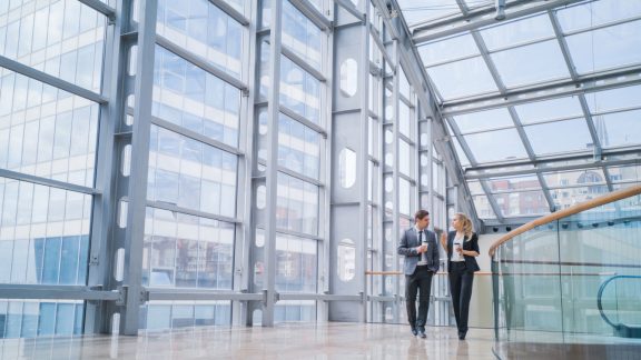 Businessman and businesswoman walk together and talk about business holding coffee in hand