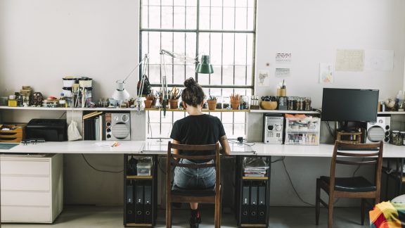 Rear view of artist working at desk. Female professional is freelancing at home. She is wearing casuals.