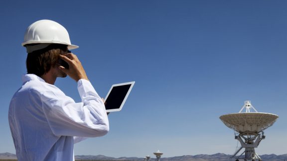 Scientist by large radio telescope array using a smart phone and tablet computer. Noise added.