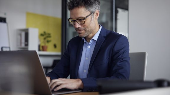 Working man wearing eyeglasses using laptop at work place