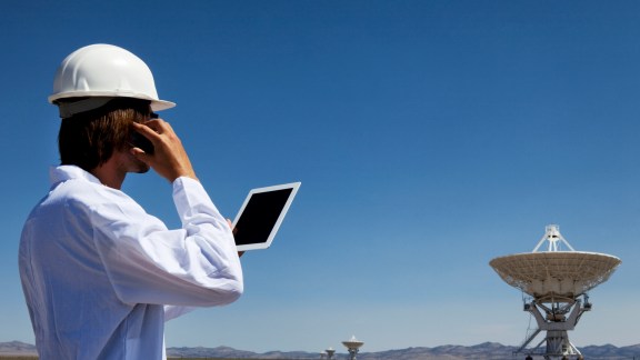 Scientist by large radio telescope array using a smart phone and tablet computer. Noise added.