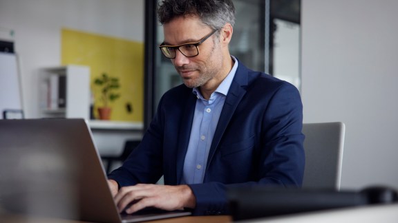 Working man wearing eyeglasses using laptop at work place