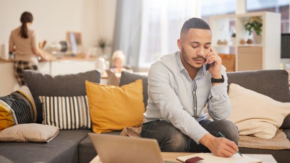 Portrait of modern mixed race man speaking by phone while working from home in cozy interior, copy space