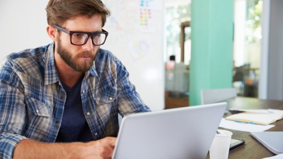 Businessman Sitting At Desk In Office Working On Laptop