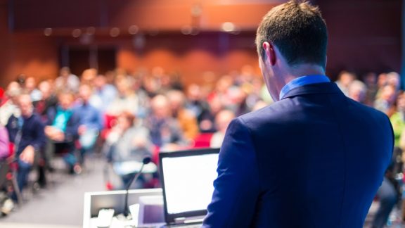 Speaker at Business Conference with Public Presentations. Audience at the conference hall. Entrepreneurship club. Rear view. Horisontal composition. Background blur.