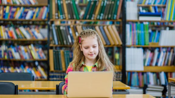 young girl with laptop working in library.