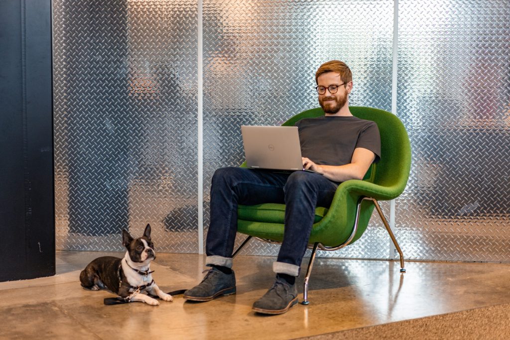 A person sitting on a chair with a computer and a dogDescription automatically generated with medium confidence