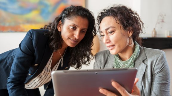 Two business women looking at a tablet computer, discussing a topic.
