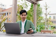 Seated man working on laptop with cell phone